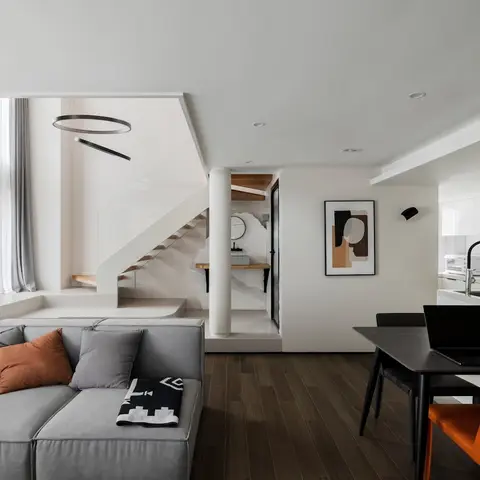 Open-plan living-dining-kitchen loft with a floating staircase, grey modular sofa with an orange throw pillow, and an orange dining chair accent.