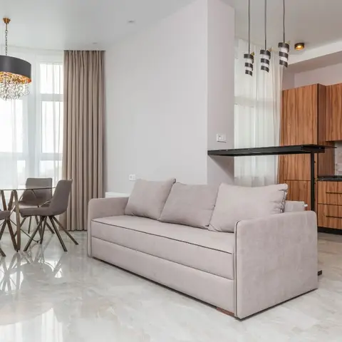 Open-plan living-dining-kitchen space with a round glass dining table under a drum chandelier, a beige sofa