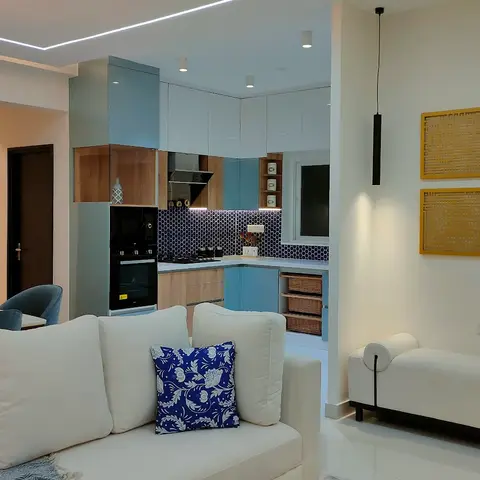 Open-plan living-dining-kitchen with a white sofa and chaise lounge in the foreground, a globe chandelier over the dining table