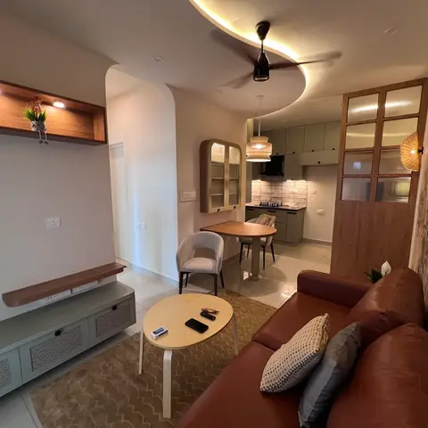 Open-plan living-dining-kitchen with a curved cove-lit ceiling, a tan leather sofa, a round dining table and sage-green kitchen cabinetry