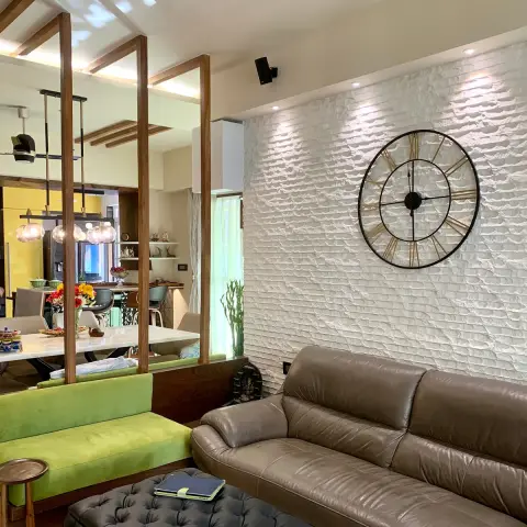 Open-plan living-dining space divided by a slatted wood partition, with a brown leather sofa against a textured white accent wall and a bright yellow kitchen