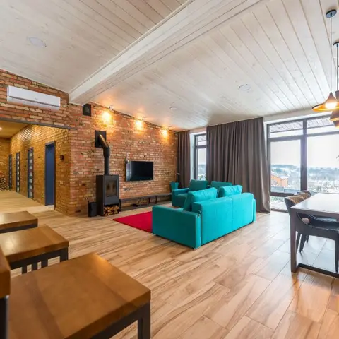 Open-plan living-dining space with an exposed red-brick wall, wood-clad ceiling, wood-burning stove
