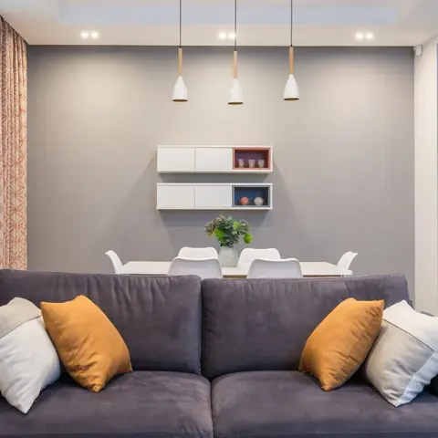 Open-plan living-dining space with a charcoal velvet sofa styled with mustard and grey cushions, a white dining set beneath three pendant lights