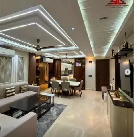 Open-plan living-dining space with a multi-tier linear-lit cove ceiling, grey L-shaped sofas around black coffee tables on a blue patterned rug