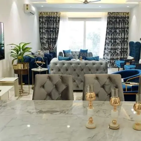 Open-plan living-dining space with a marble-top dining table and tufted grey chairs in the foreground