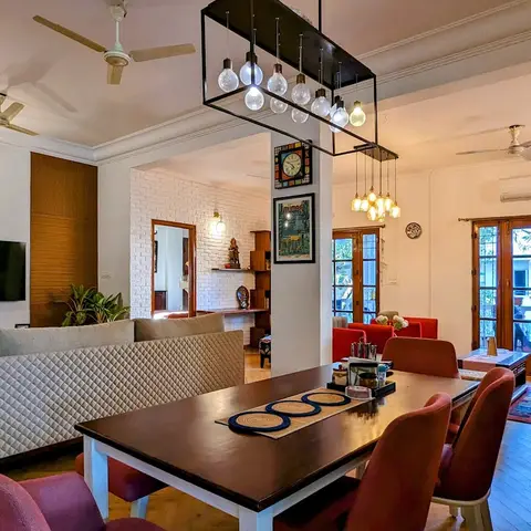 Open-plan living-dining space with a quilted grey sofa, mismatched pink and red dining chairs, a cage-style multi-bulb pendant