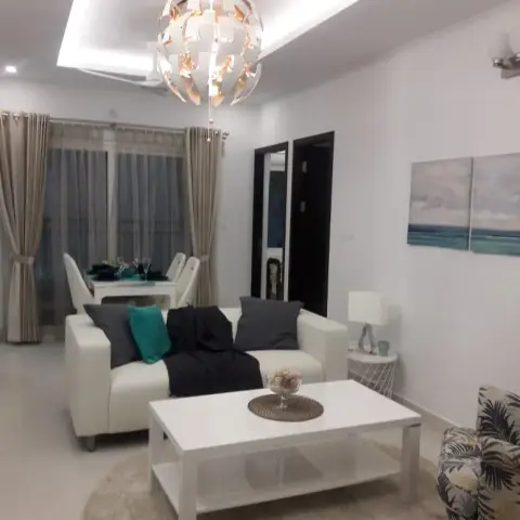 Open-plan living-dining space with a sculptural white pendant light, a cream sofa with teal and charcoal cushions, and ocean-themed wall art