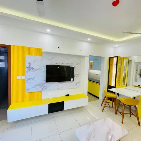 Open-plan living-dining space with a marble-panel TV wall accented by yellow fluted panelling, a yellow-and-white dining nook with bar stools