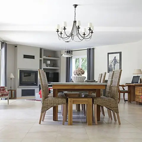 Open-plan living-dining-study space with a rattan-chair dining set under a candelabra chandelier, a fireplace lounge with red accent chairs on the left
