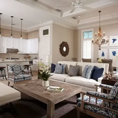 Open-plan living-kitchen-dining space with a reclaimed-wood coffee table, navy-and-white patterned armchairs, a beaded chandelier over the dining table