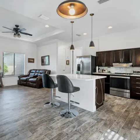 Open-plan living-kitchen with espresso raised-panel cabinets, a white quartz island on two chrome bar stools