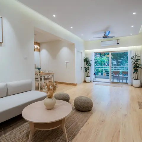 Open-plan living room with a light-grey sofa, round wood coffee table, woven poufs and a jute rug on light wood-plank flooring, opening onto a balcony
