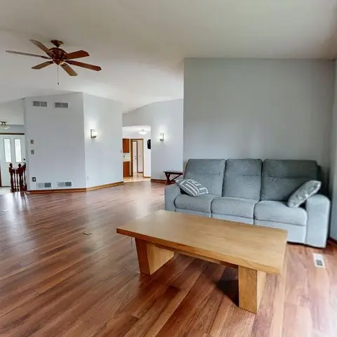 Open-plan living room with wide-plank wood flooring, a vaulted ceiling fan, and a grey sofa facing a wood coffee table.