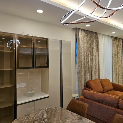 Open-plan living space with a mirrored glass-front display cabinet, floral curtains, a sculptural ribbon pendant light