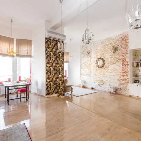 Open-plan loft apartment with a kitchenette and dining nook to one side, an exposed brick feature wall with a sunburst mirror