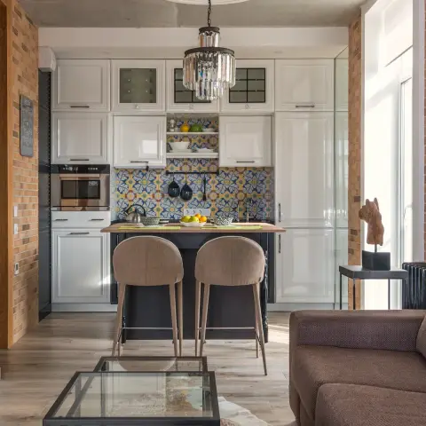 Open-plan loft flat where a white raised-panel kitchen with a blue-and-yellow azulejo backsplash sits under a raw concrete slab