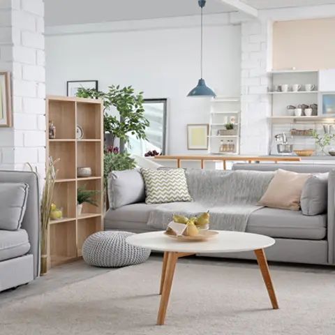 Open-plan Scandinavian-style living-kitchen with white brick columns, a grey linen L-shaped sofa, round wood-legged coffee table, open wood shelving unit