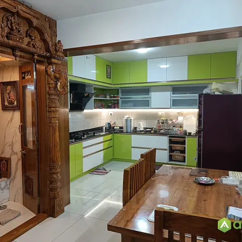 Open-plan shot showing an elaborately hand-carved wooden pooja mandap on the left, a lime-green and white gloss L-shaped modular kitchen straight ahead