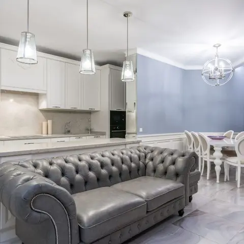 Open-plan space combining a white shaker-style kitchen, a tufted grey leather chesterfield sofa on a kitchen island