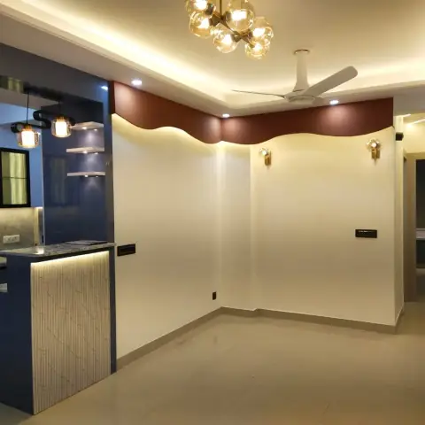Open-plan space showing a navy modular kitchen counter beside an empty living area with a wave-profile cove-lit ceiling cornice in maroon.