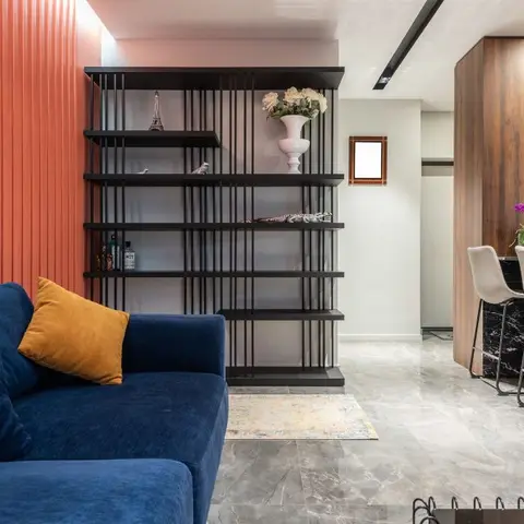 Open-plan space with a navy velvet sofa against a coral fluted wall, a black ladder-style display shelf, and a wood-clad bar counter with stools visible beyond