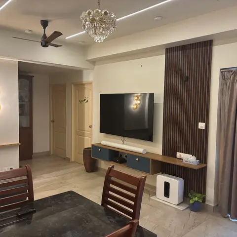 Open-plan view of a dining table in the foreground and a living room TV wall with fluted wood panelling beyond, both visible with no single zone dominant