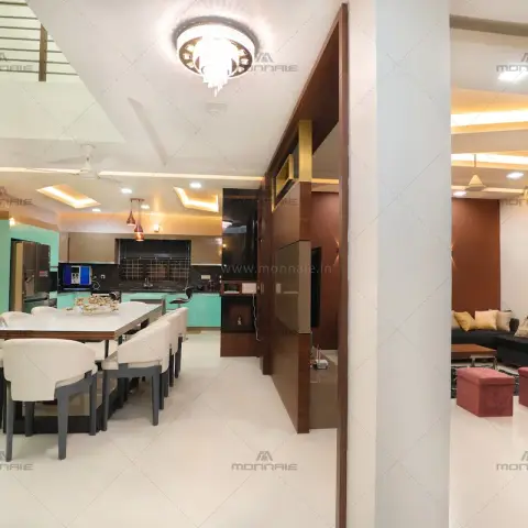 Open-plan villa floor with a long white ten-seat dining table under a crystal drum fitting, a mint-green kitchen behind it