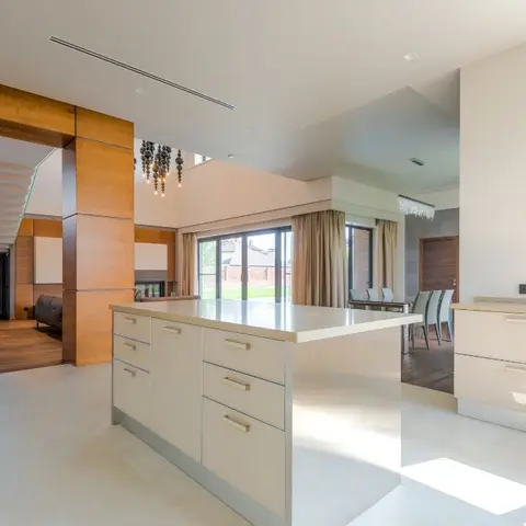 Open-plan villa interior with a white kitchen island, a glass-walled dining area with sheer curtains