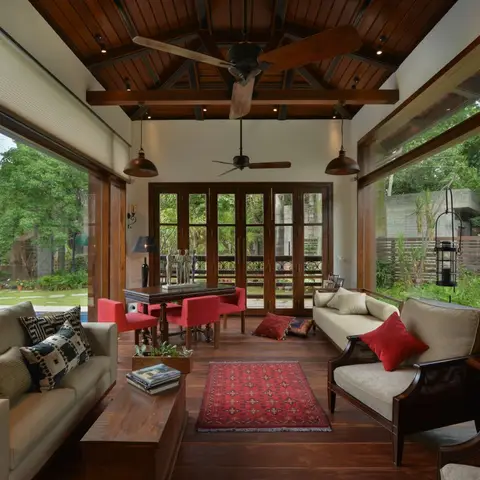 Open veranda living room with an exposed wood-beam vaulted ceiling, bell pendant lights, colonial cane armchairs