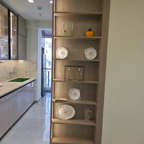 Open wood-veneer display shelving with LED strip lighting and styled crockery, standing at the kitchen entrance with counter and sink visible beyond.