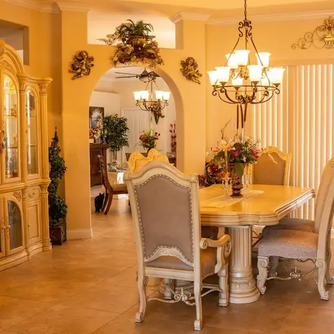 Ornate carved-wood dining set with nailhead-trimmed upholstered chairs beneath a wrought-iron chandelier