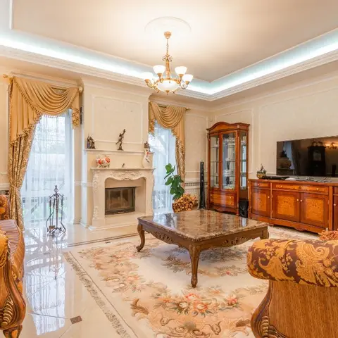 Ornate classic living room with a marble fireplace surround, a crystal chandelier, and gold damask-upholstered sofas around a carved wood coffee table.