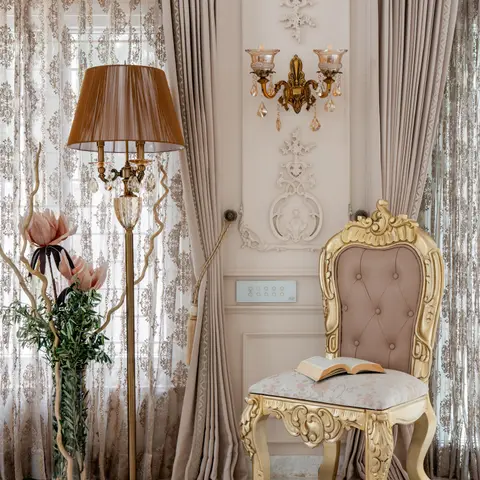 Ornate corner with a gilt carved rococo chair and stool, a crystal floor lamp, and detailed plaster wall moulding beneath a crystal wall sconce.