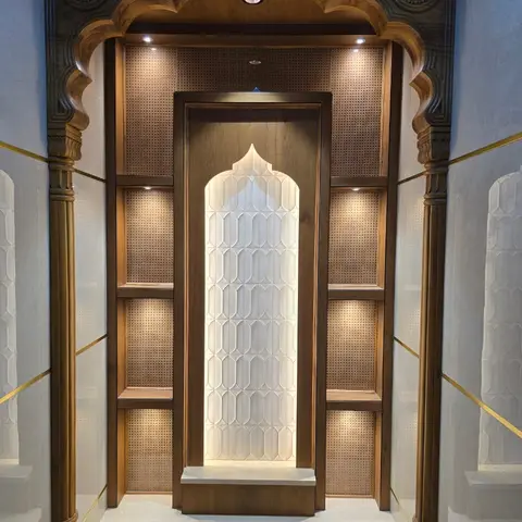 Ornate pooja room with a hand-carved wood jharokha-style arch, a backlit marble jaali screen and cane-panelled side niches.