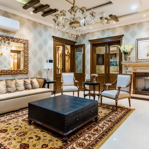 Ornate traditional living room with a crystal chandelier, a carved marble fireplace mantel and a large amber-mosaic framed mirror above a cream sofa.