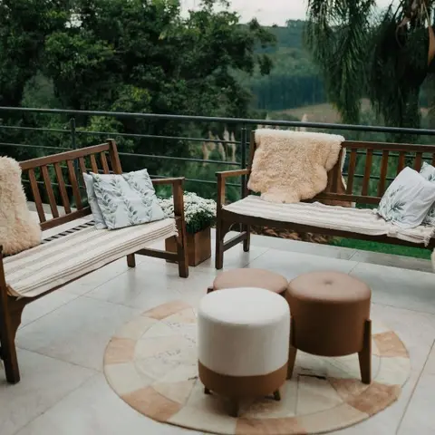 Outdoor terrace seating with two wood-slat benches dressed in sheepskin throws and striped cushions, round ottomans on a patterned rug