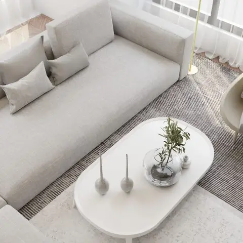 Overhead view of a grey L-shaped sofa with bolster cushions beside an oval white coffee table styled with candlesticks and a potted olive branch