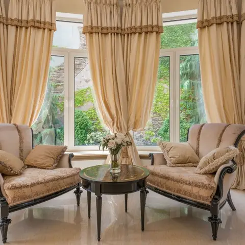 Pair of tufted cream armchairs with dark carved wood trim flanking a round black coffee table with fresh flowers