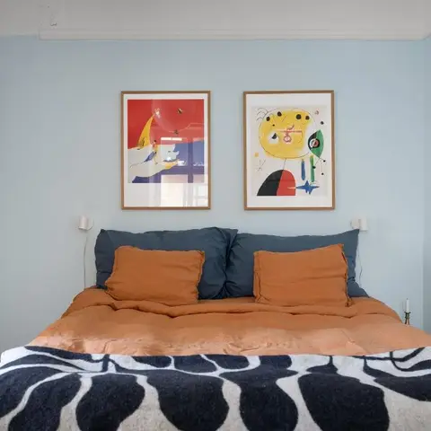 Pale blue bedroom with a pair of framed Miro-style prints hung centred above terracotta linen bedding and slate-blue pillows