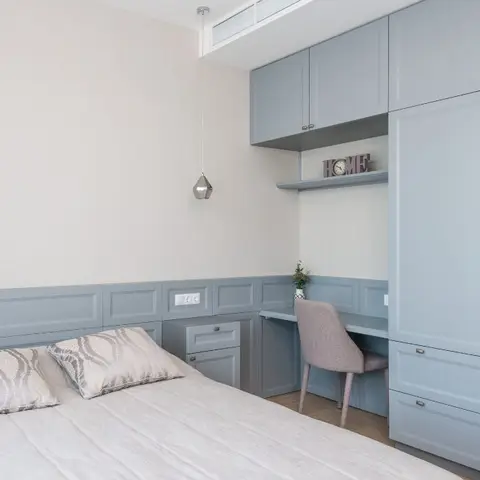 Pale blue shaker-fronted joinery wraps this bedroom - the dado panelling behind the bed turns into a desk nook with an open shelf and overhead lockers