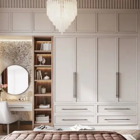 Panel-moulded wardrobe wall with a crystal chandelier, alongside a backlit stone-effect dressing nook with a round mirror and blush bedding visible in the