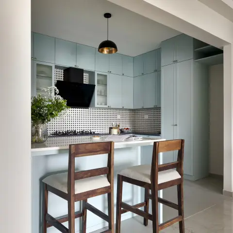 Pastel blue shaker-style kitchen with a black-and-white geometric mosaic backsplash, a black-and-brass dome pendant light over the breakfast counter