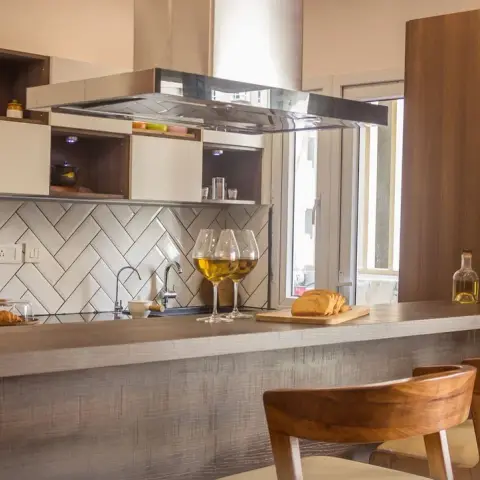 Peninsula kitchen where a white herringbone subway backsplash runs behind the sink, under a mirror-finish island chimney