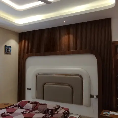 Phone snapshot of a bedroom where three stepped rounded-corner upholstered headboard frames are set into a full-height fluted teak wall