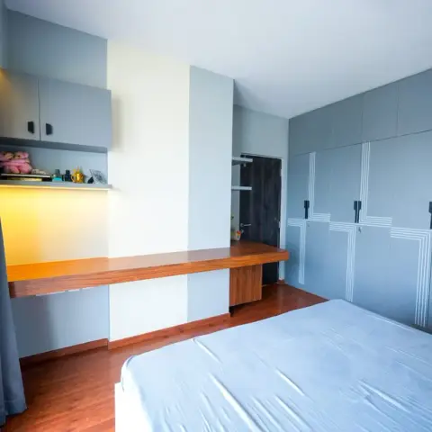 Photo of a bedroom where a long teak desk ledge runs the wall under a backlit display shelf and overhead cabinet