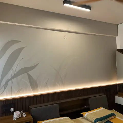 Photo of a bedroom where a concealed LED strip along the top of a dark fluted dado grazes a pale grass-and-leaf mural