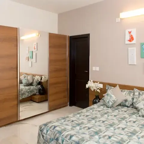 Photo of a bedroom where a teak sliding wardrobe with a central mirror shutter faces a bed whose headboard is a teak band carried across the wall