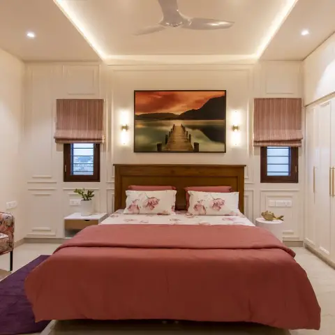 Photo of a bedroom with a teak headboard and dusty-rose bedding, ivory moulded wall panels behind it
