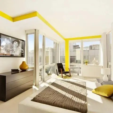 Photo of a bright corner bedroom where a yellow painted band traces the ceiling edge and drops down a window pier
