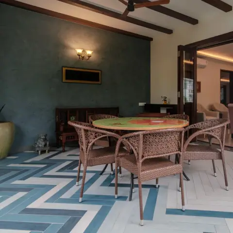 Photo of a covered sit-out floored in blue and white herringbone tile, with a cane dining set around a painted round table